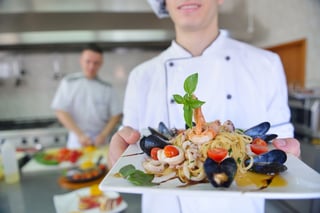 Handsome chef dressed in white uniform decorating pasta salad and seafood fish in modern kitchen.jpeg