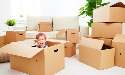 Child sitting in a cardboard box in a room filled with boxes